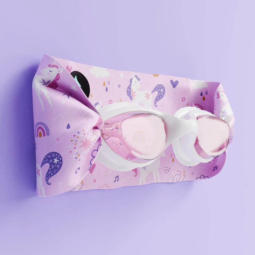 Óculos de natação Waterplops brancos com lentes cor-de-rosa, dobrados e parcialmente cobertos pela sua bolsa de tecido com estampa de unicórnios.