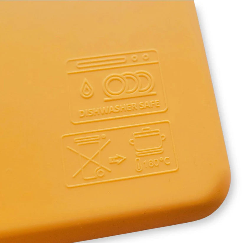 Close-up no silicone amarelo do Wiggly Toy, mostrando os símbolos de "Lavável na máquina de lavar loiça" e resistência térmica até 180ºC.