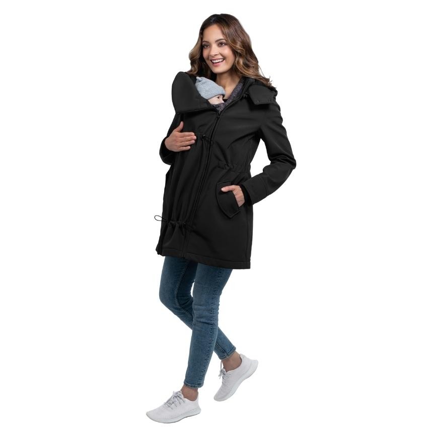 Mulher sorridente com casaco Wombat Shell preto, a usar o painel de transporte para segurar um bebé virado para a frente.