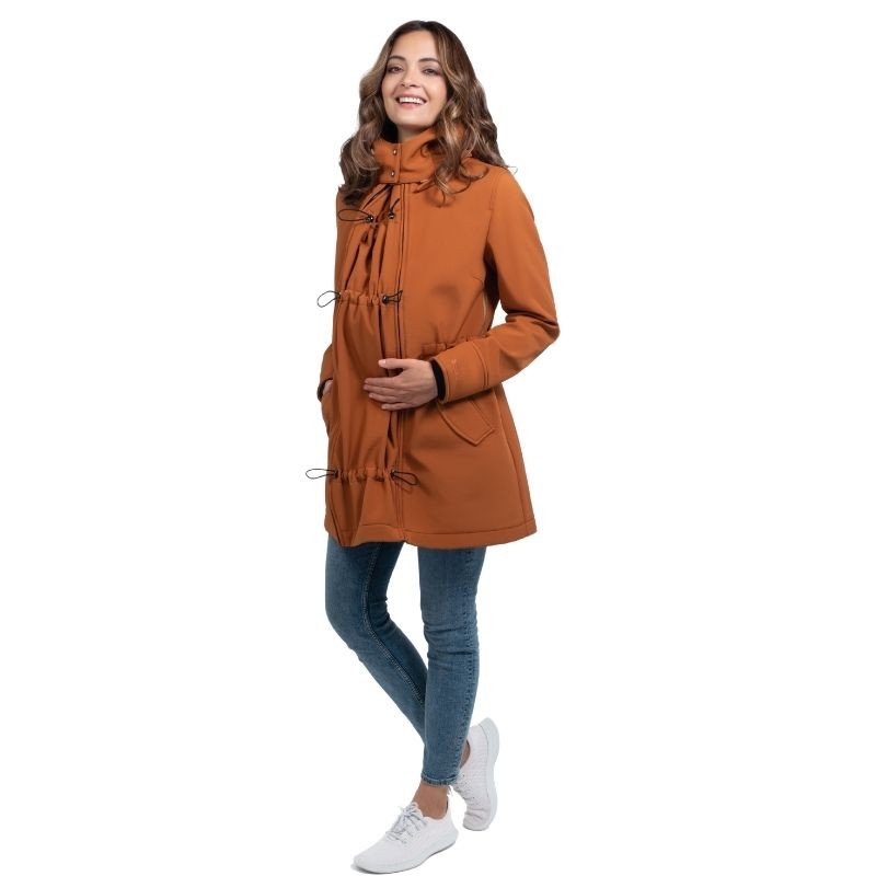 Mulher sorri, de corpo inteiro, vestindo o casaco Wombat Shell caramelo com o painel de transporte removido, em fundo branco.