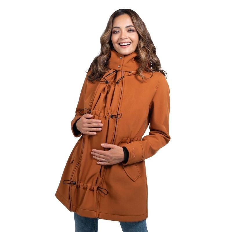 Mulher sorri, mostrando o casaco Wombat Shell caramelo ajustado à barriga de grávida com cordões de ajuste visíveis.