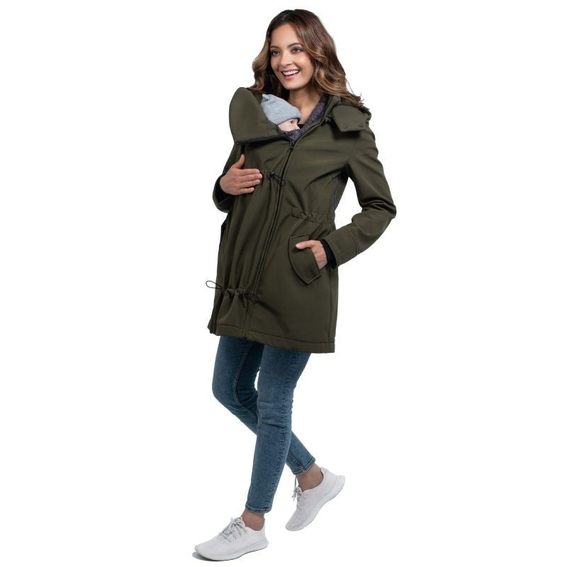 Mãe sorridente a usar o casaco Wombat Shell verde com painel de transporte, segurando um bebé no peito, em fundo branco.