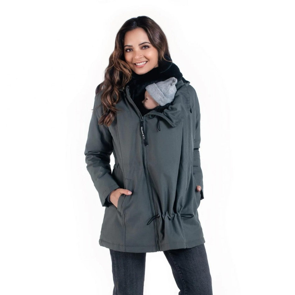 Mulher sorridente com o casaco Wombat Wallaby cinzento, a usar o painel de transporte frontal com um bebé aninhado.