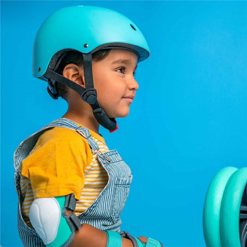 Criança a usar capacete azul Yvolution com joelheiras a condizer em fundo azul.