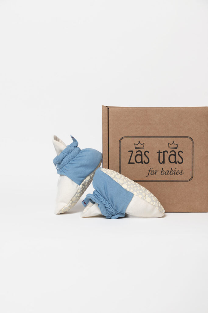 Pantufas botinhas de bebé Zás Trás 'Blue PopCorn' ao lado da sua embalagem de cartão com o logótipo da marca.