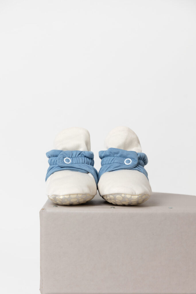 Vista frontal das pantufas botinhas de bebé Zás Trás, em azul e branco, assentes numa caixa, destacando o fecho de mola de pressão.