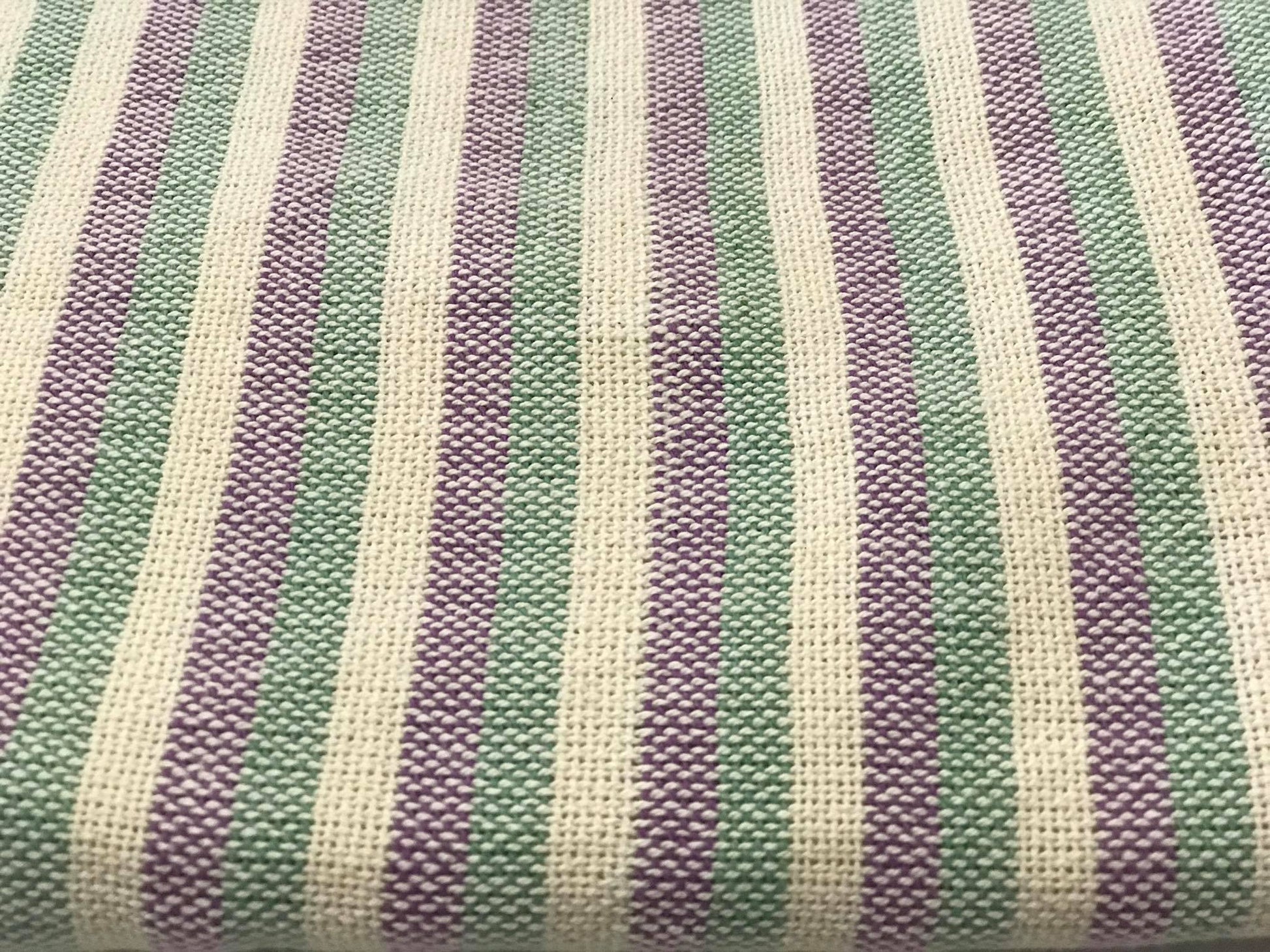Detalhe de um pano tecido com riscas em tons de rosa e verde, mostrando a textura e a qualidade do tecido.