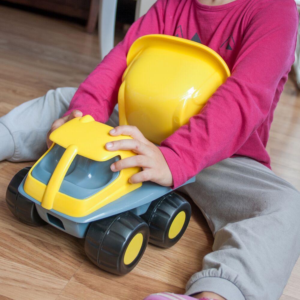 Criança sentada no chão de madeira a brincar com o camião Miniland Amarelo, segurando-o com as duas mãos.