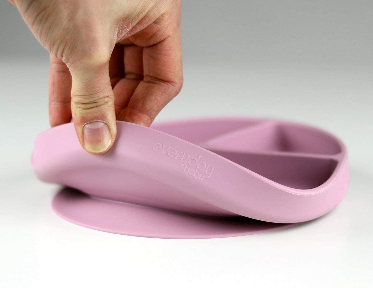 Mão a levantar um prato de silicone rosa da Everyday Baby, mostrando a base com ventosa e a flexibilidade do material.