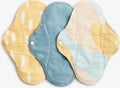 Conjunto de três pensos menstruais reutilizáveis ImseVimse Dia SPRINKLE em tons de amarelo, azul e bege com padrões abstratos e botões de pressão brancos.