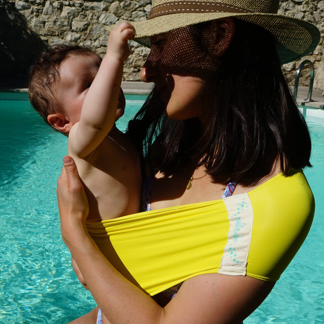 Mulher na piscina segurando um bebé com o Pouch Sling Neobulle Aquabulle em amarelo.