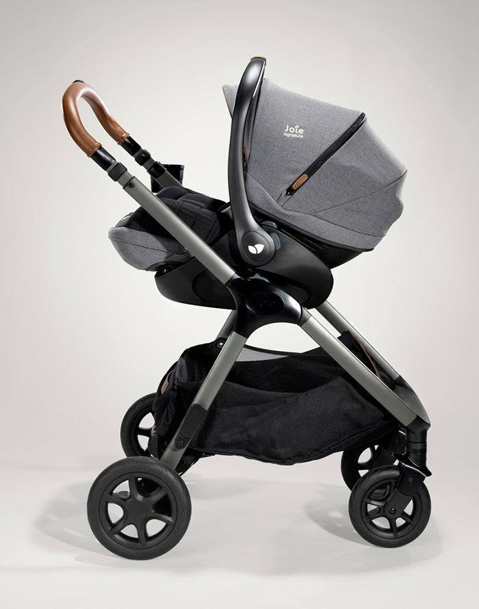 Vista lateral da cadeira auto i-Size instalada num carrinho, destacando a alça de transporte e a estrutura robusta.