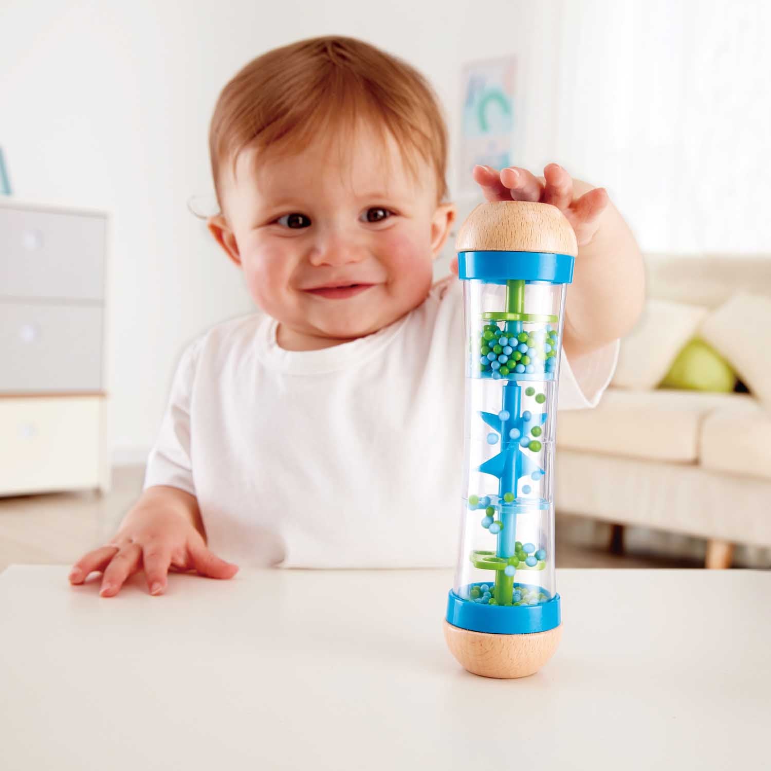 Bebé sorridente a segurar o Hape Pau de chuva azul, mostrando a sua interação com o brinquedo sensorial.