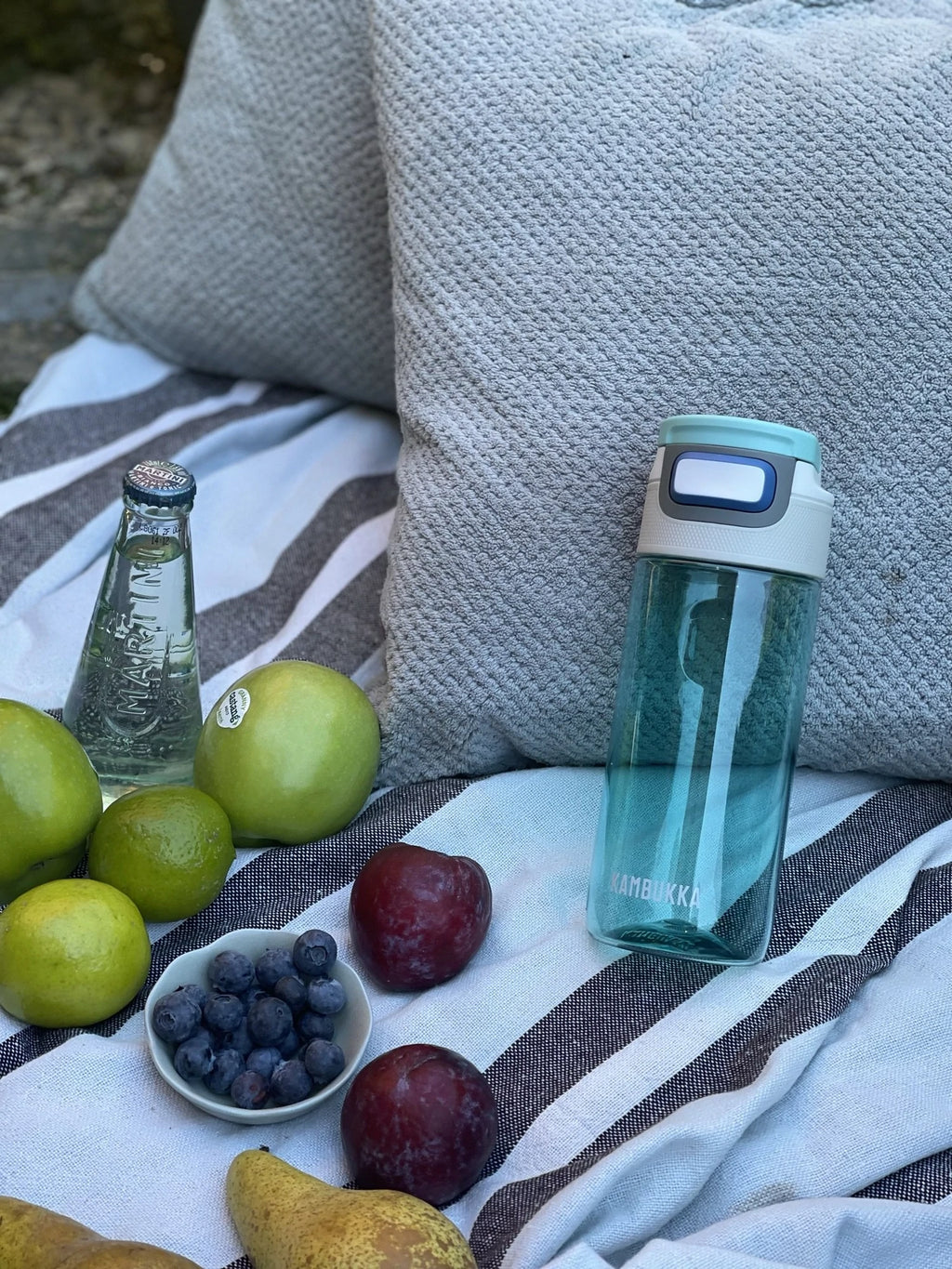 Garrafa Kambukka Elton 500ml verde água cheia de água, em cenário de piquenique com frutas e bebidas.