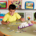 Criança sorridente a jogar com o Miniland Jogo Educativo de Sequências, organizando cartas numa base roxa.