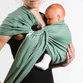 Homem a usar um sling de argolas Neobulle Vert Eucalyptus, com um bebé posicionado na frente do seu corpo, mostrando a forma como o sling envolve o corpo do bebé.