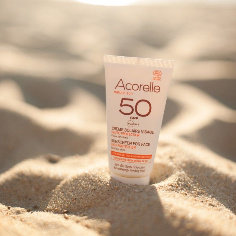 Tubo de protetor solar Acorelle SPF50+ colocado sobre a areia da praia num ambiente ensolarado.