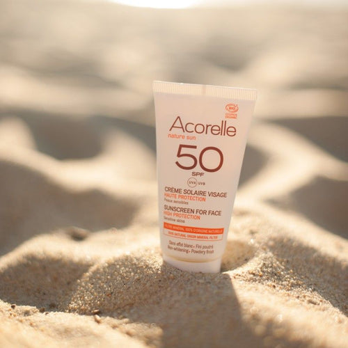 Tubo de protetor solar Acorelle SPF50+ colocado sobre a areia da praia num ambiente ensolarado.