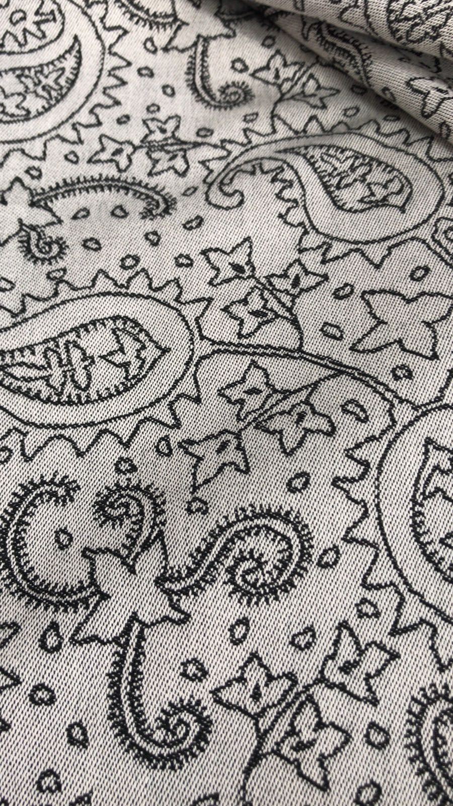 Close-up de tecido cinzento claro com padrão paisley preto, mostrando a textura e os detalhes do desenho para aluguer de porta-bebés.