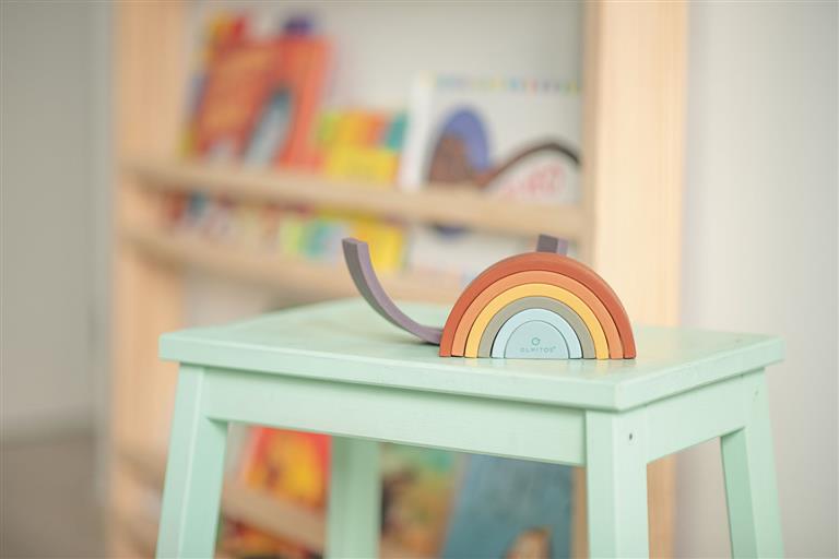 O arco-íris de silicone Olmitos num ambiente infantil, sobre uma pequena mesa, mostrando o brinquedo no contexto de brincadeira.
