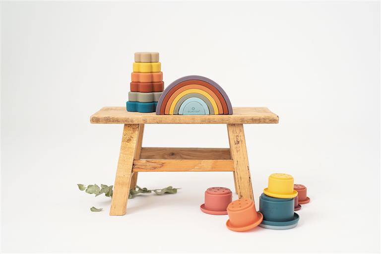 O arco-íris de silicone Olmitos e outros brinquedos de silicone Olmitos numa mesa de madeira, mostrando a variedade de produtos da marca.