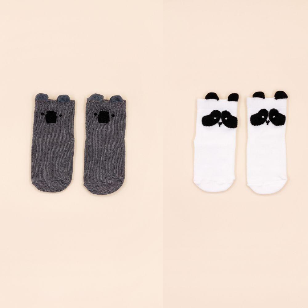 Comparação de dois pares de meias Attipas: um par cinzento com cabeça de urso e um par branco com cabeça de panda, dispostos lado a lado sobre fundo bege.