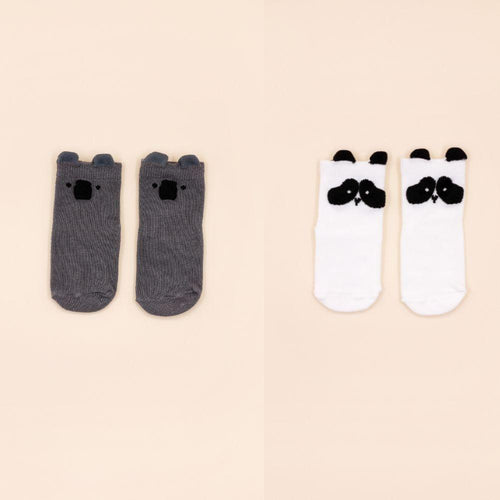 Comparação de dois pares de meias Attipas: um par cinzento com cabeça de urso e um par branco com cabeça de panda, dispostos lado a lado sobre fundo bege.