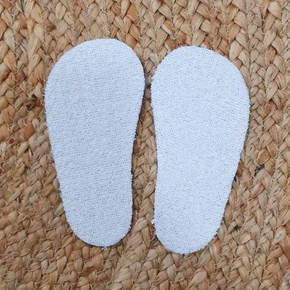 Par de palmilhas Attipas brancas com superfície felpuda visível, focadas no controlo de humidade, sobre fundo de fibra natural.