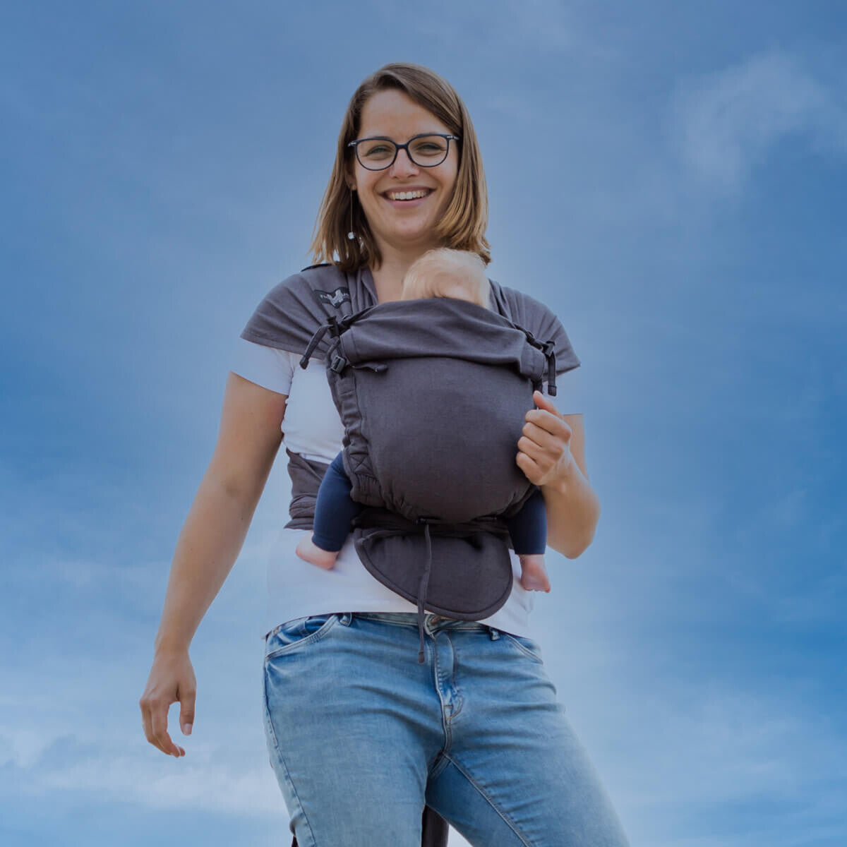 Mulher a usar o Mei Tai Hoppediz com bebé, destacando o ajuste confortável e seguro do porta-bebés.