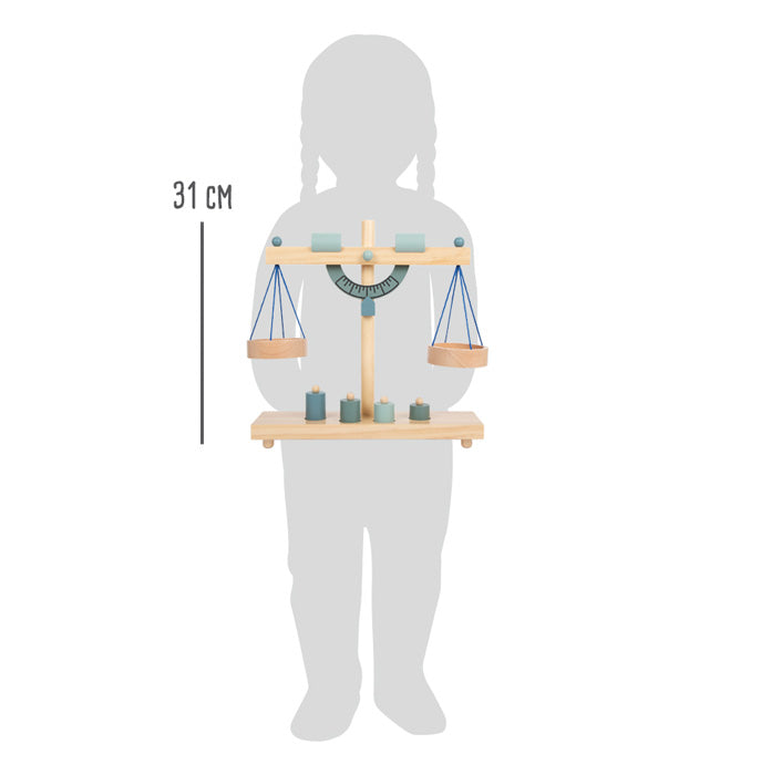 Imagem que mostra as dimensões da balança de madeira small foot (31 cm de altura) em comparação com uma criança, para melhor visualização do tamanho.