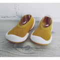 Par de Banannas Baby Shoes em amarelo mostarda com sola branca e detalhes arredondados. O design flexível e tipo meia proporciona máximo conforto, aderência e liberdade de movimento, ideal para bebés em fase de crescimento.

