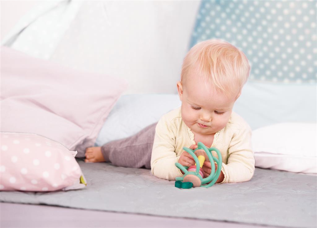 Bebé a brincar com o Hape Maça espiral em cima de uma cama