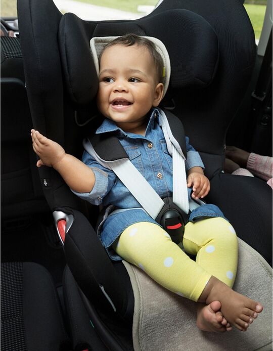 Bebé sorridente sentado numa cadeira auto Grupo 1, com a capa anti transpirante instalada, mostrando conforto durante a viagem.