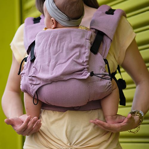 Bebé transportado confortavelmente numa mochila Neko Switch "Cotton Candy", com o assento em forma de M visível, garantindo suporte ergonómico.