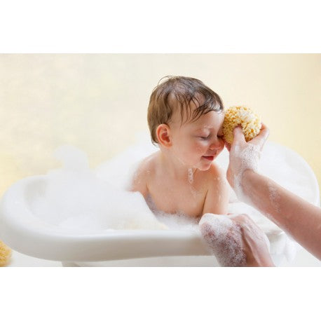 Mãe a dar banho a bebé com esponja natural Beliini, bebé sorrindo e relaxado na banheira com espuma.