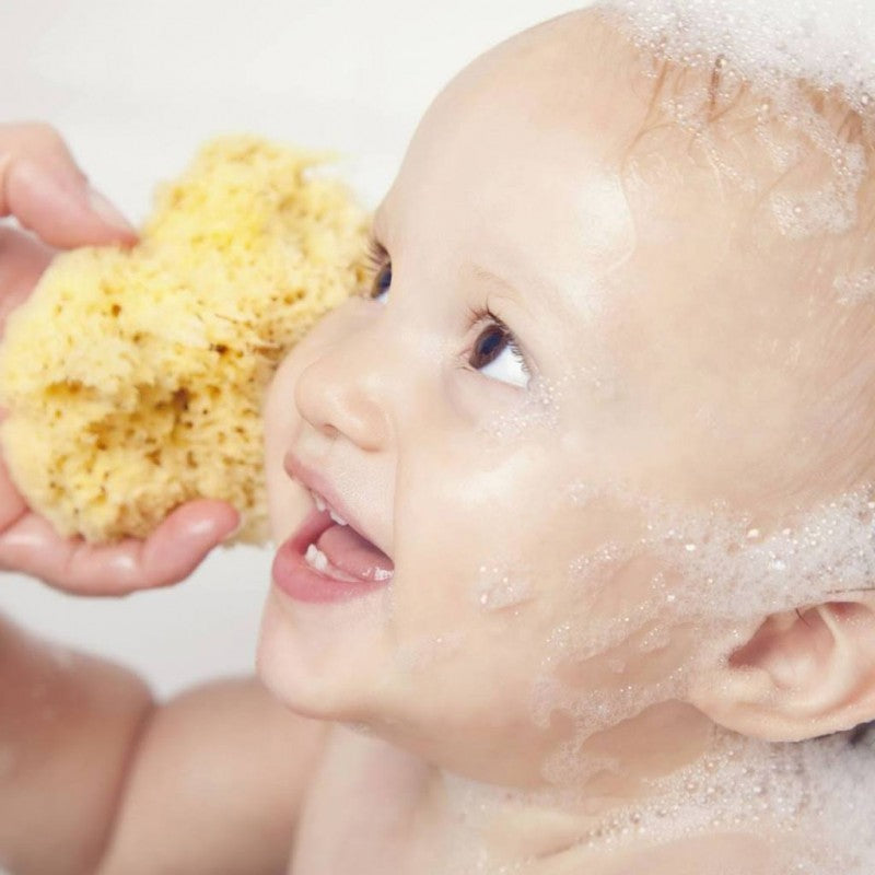 Close-up de bebé a receber banho com esponja natural Beliini, pele macia e sorrindo durante o banho.