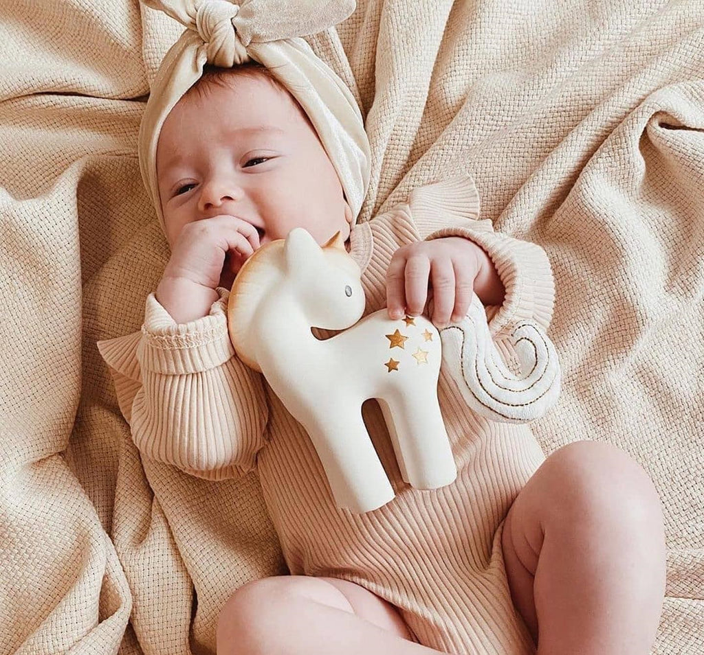 Bebé com um mordedor em forma de unicórnio. Descubra a nossa coleção de brinquedos de estimulação para recém-nascidos.