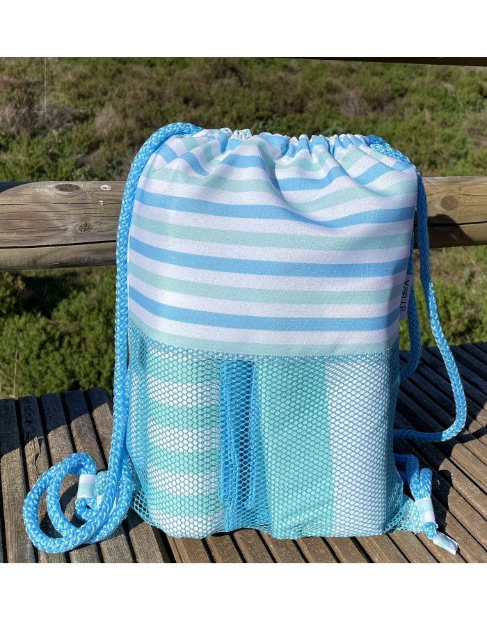Mochila Btbox sem areia, com riscas azuis e brancas, em primeiro plano, com bolso de rede azul a conter algo, pousada sobre uma estrutura de madeira exterior.