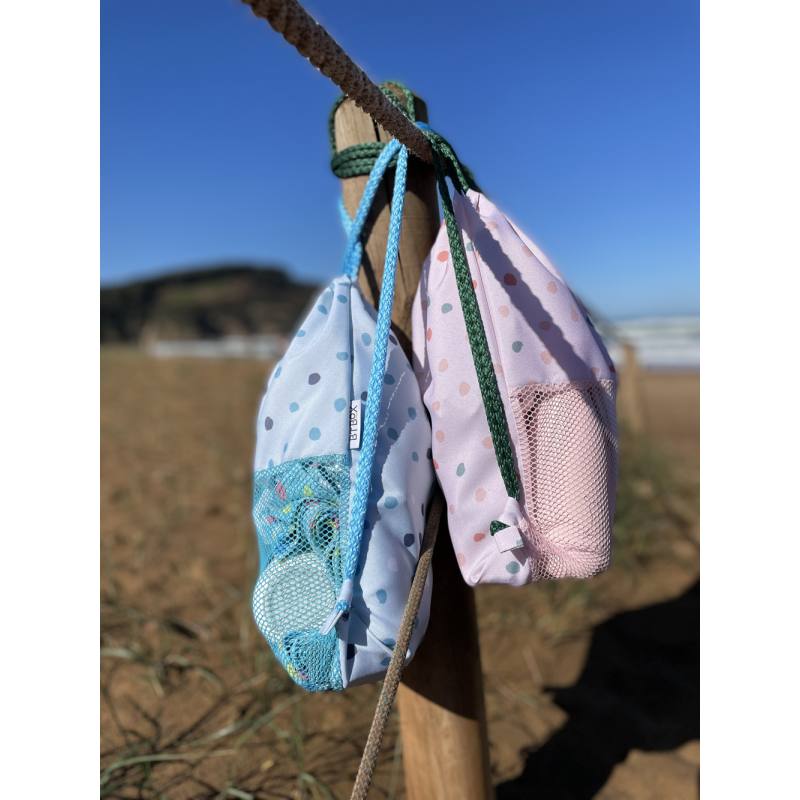 Imagem da mochila Btbox ao lado de uma toalha de praia e um fato de banho, ilustrando o seu uso prático em ambiente de lazer.