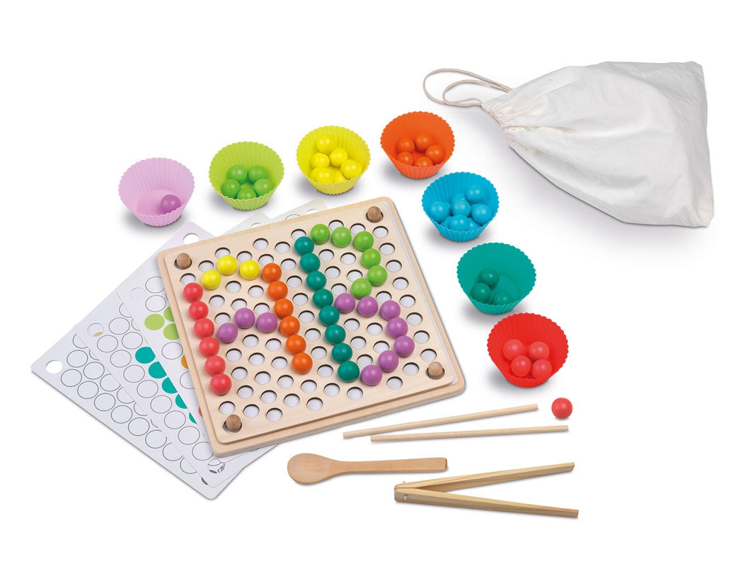 Componentes do jogo Cayro Contas e Cores Beads and Clip dispostos numa mesa, incluindo o tabuleiro, as contas coloridas, os clipes, os paus e a colher.