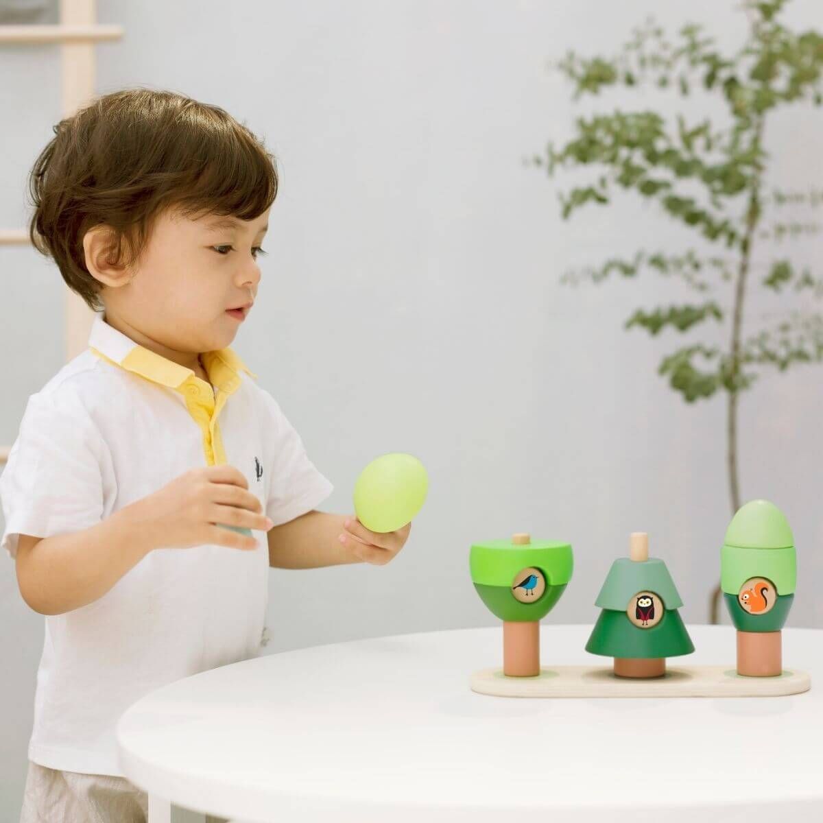 Criança brincando com as árvores de jardim empilháveis Classic World, um brinquedo educativo de madeira para desenvolver a imaginação.
