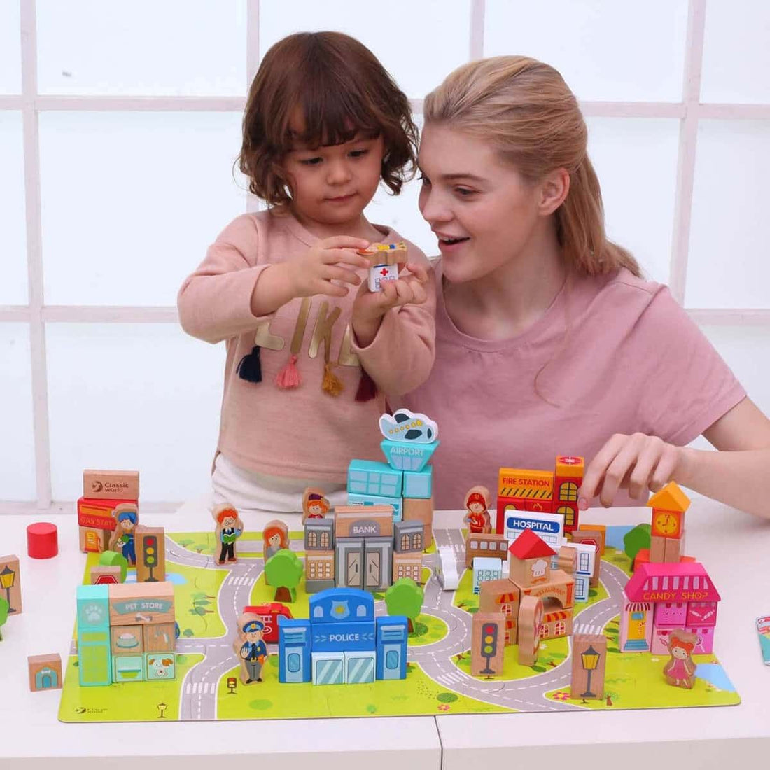 Visão geral do conjunto Classic World Blocos de Construção 'Cidade', mostrando diversos edifícios, figuras e peças de puzzle num tapete com estradas.