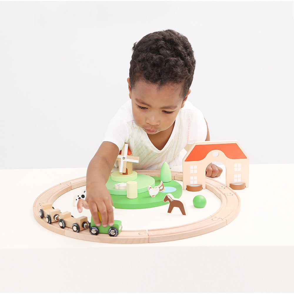 Criança brincando com o Classic World Conjunto de Comboio com Pista, explorando a quinta e o moinho de vento de madeira.