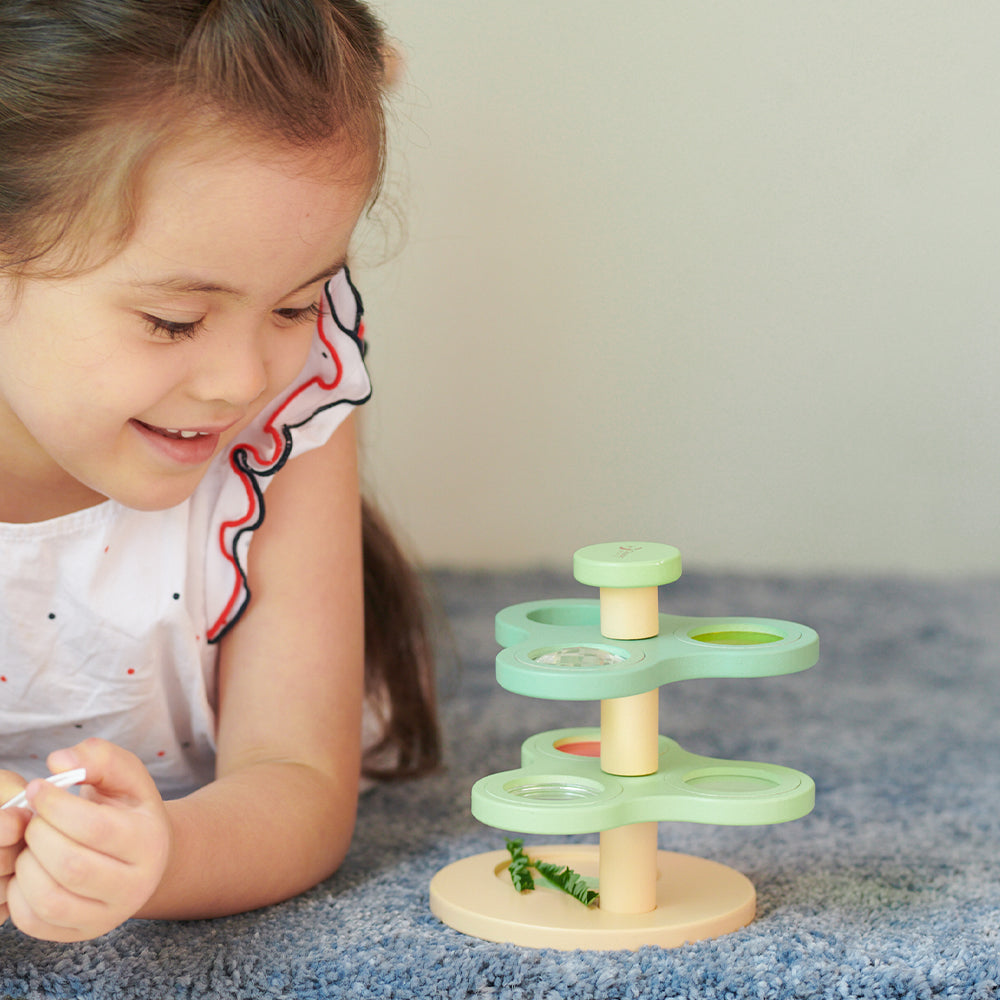 Criança brincando com o brinquedo educativo Classic World Lupa e Prismas Visuais no chão.