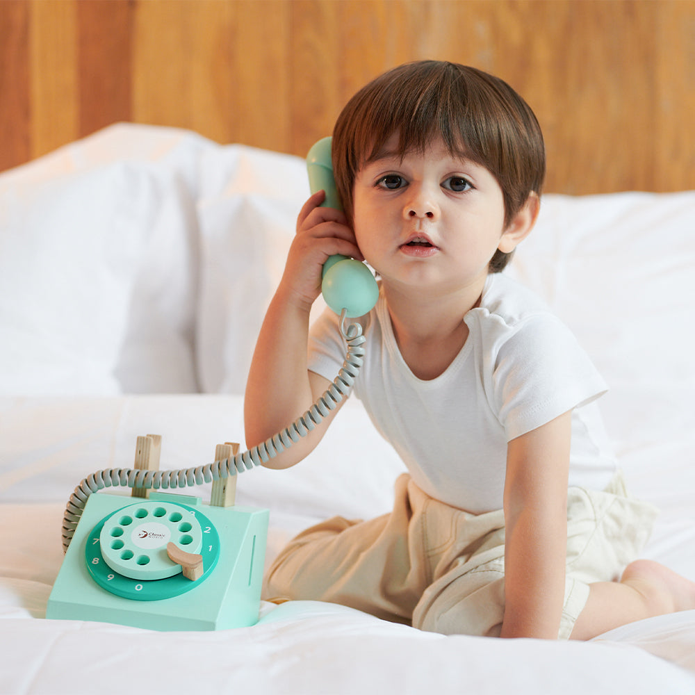 Criança a brincar com o telefone vintage de madeira, simulando uma chamada, focando na interação e no desenvolvimento motor.