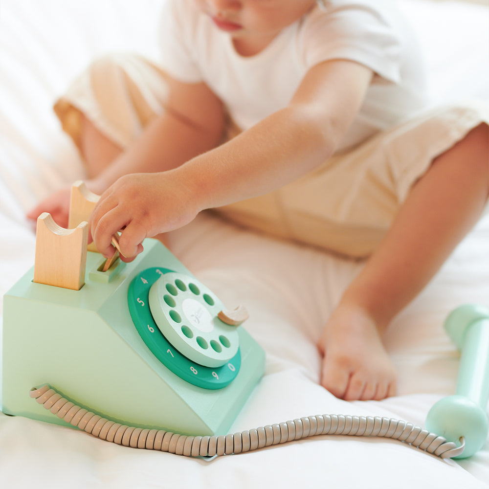 Telefone de brincar vintage Classic World em madeira, cor creme e vermelho, com disco rotativo e ranhura para moedas.
