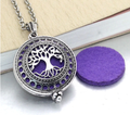 Colar difusor pessoal prateado com medalhão recortado com o padrão da Árvore da Vida ao lado de uma almofada de feltro roxa.