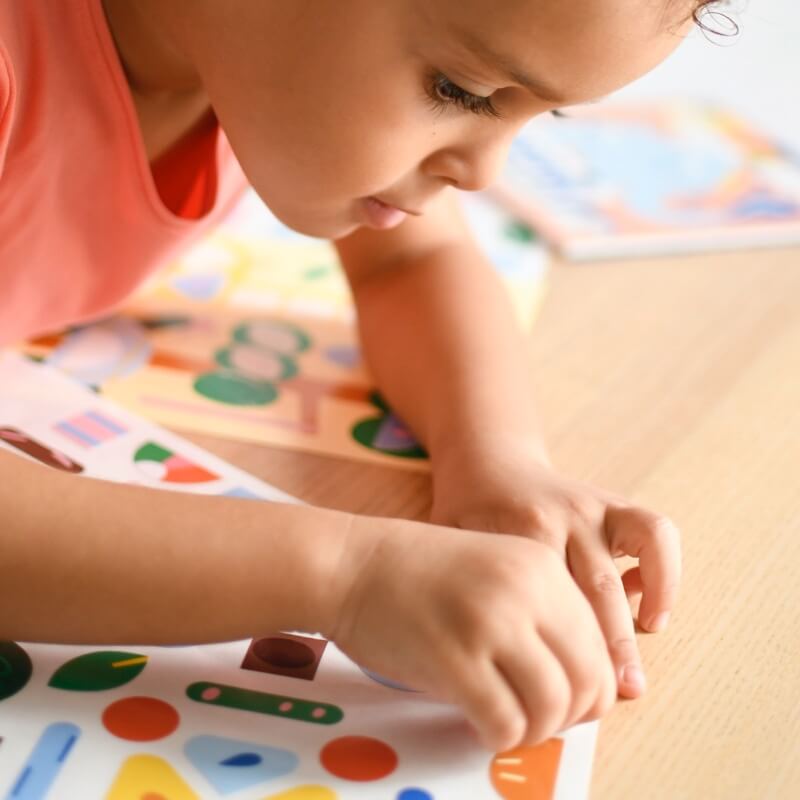 Menina concentrada a colar autocolantes geométricos no cartão ilustrado