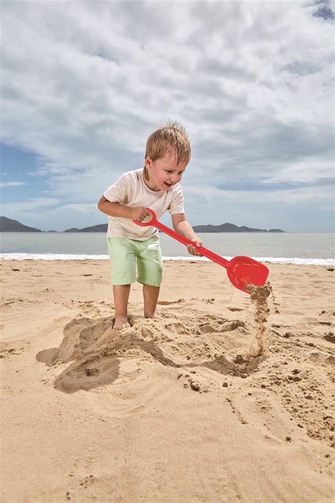 Criança a brincar com pá de praia vermelha Hape na areia