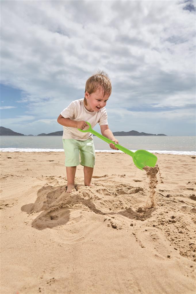 Criança a brincar na areia da praia com uma pá verde da marca Hape